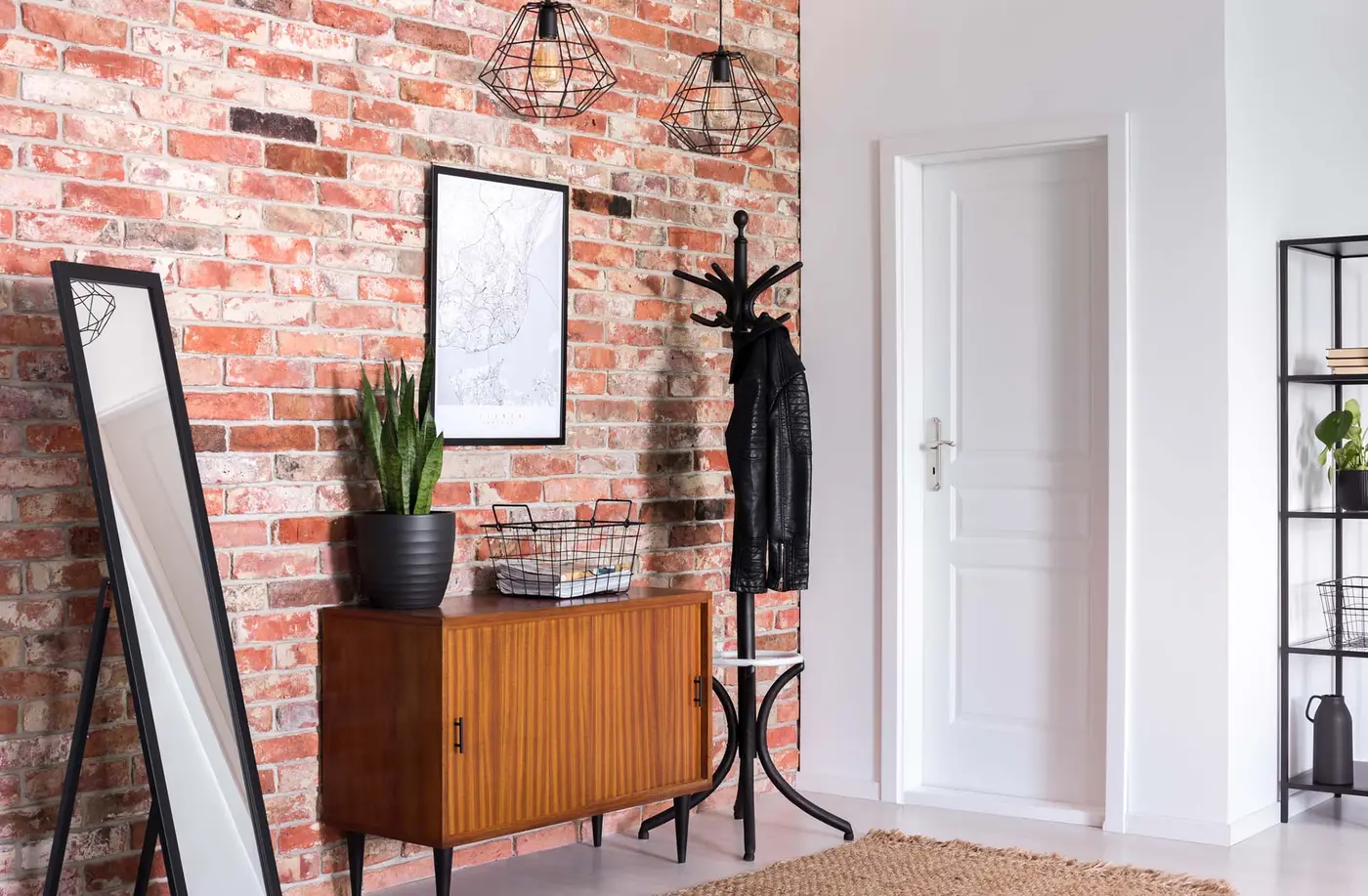 Mirror next to wooden cabinet in entrance hall interior with white door and poster on red brick wall. Real photo
